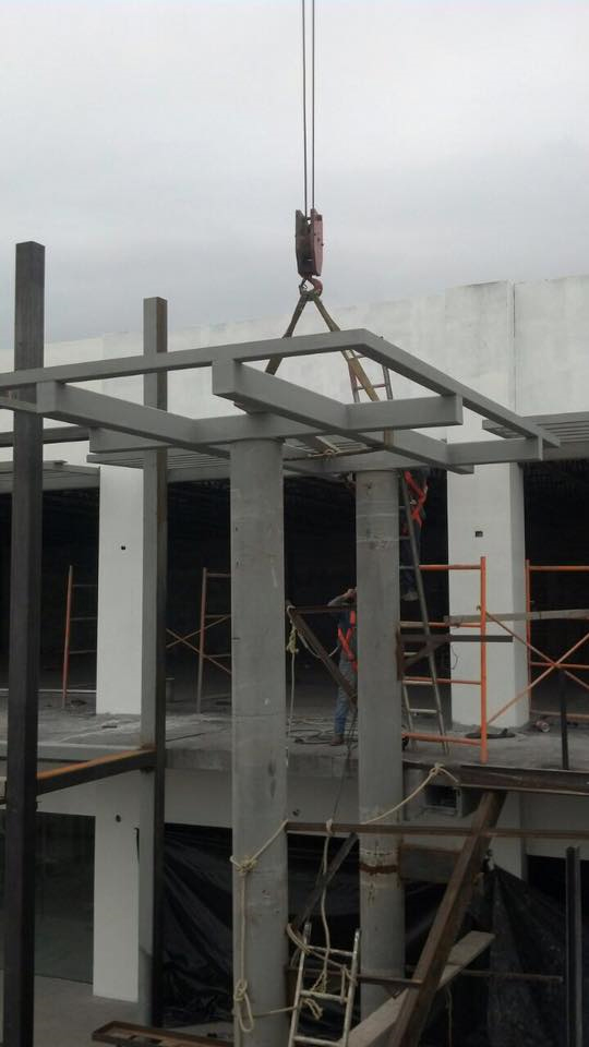 Izaje de estructura metálica de escaleras mediante grúa durante el proceso de montaje en edificio comercial.